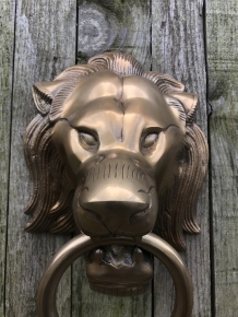 A lion's head, made of aluminum in a brass color, as a door knocker